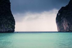 two large rocks sticking out of the ocean next to each other in front of an overcast sky