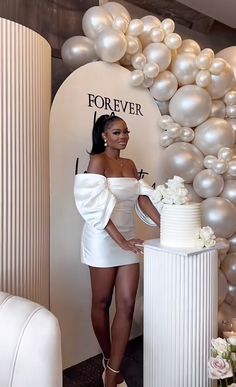 a woman standing in front of a cake with balloons behind her and holding a knife