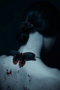 the back of a woman's neck with a butterfly on her left shoulder and blood all over it