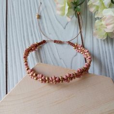 a pink beaded bracelet sitting on top of a wooden table next to flowers and a vase