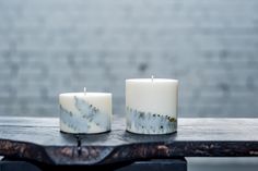 two white candles sitting on top of a wooden table next to each other with black and white designs