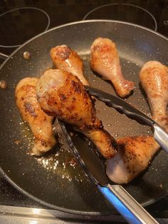 some chicken is cooking in a frying pan with tongs on the stove top