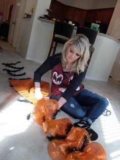 a woman sitting on the floor in front of some orange mesh bags with black bats