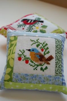 two decorative pillows sitting on top of a white table next to each other, one has a bird and the other has berries