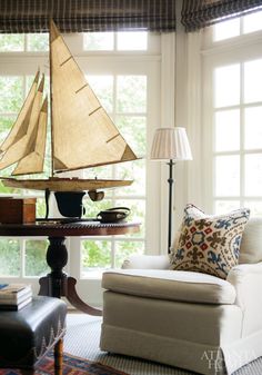 a living room filled with furniture and a sail boat on top of a table next to a window