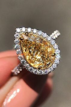 a fancy yellow diamond ring is being held by someone's hand in front of the camera