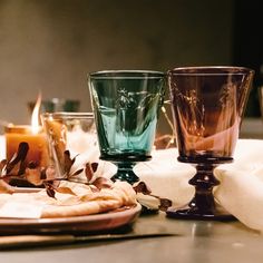 three glass cups sitting on top of a table next to candles and plates with napkins