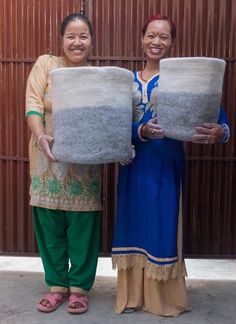 two women standing next to each other holding up large pots in front of a wall