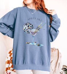 Celebrate your love for skiing and après ski festivities with this chic and playful sweatshirt! Featuring a stylish martini glass with crossed skis and a disco ball, this design embodies the fun and relaxation of après ski moments. Perfect for ski enthusiasts and cocktail lovers alike, this sweatshirt will keep you warm and stylish whether you're lounging by the fire after a day on the slopes or heading to a winter party. Crafted from soft, cozy fabric, this sweatshirt is ideal for layering during ski season or for casual winter wear. How To Order 1. Please, check and review all photos. 2. Select your Sweatshirt size and color. 3. Click add to cart. Continue shopping for free shipping! ($35 minimum) 4. If finished, Click "Proceed to check out" to finalize.  5. Carefully review all items as Long Sleeve Sweatshirt For Winter Sports, Casual Winter Skiing Tops, Long Sleeve Ski Tops For Ski Season, Long Sleeve Skiing Tops For Ski Season, Long Sleeve Tops For Ski Season And Winter Sports, Long Sleeve Tops For Ski Season, Casual Skiing Tops, Casual Crew Neck Sweater For Ski Season, Casual Graphic Print Tops For Winter Sports