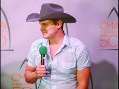 a man wearing a cowboy hat holding a microphone in front of a purple wall with the words cma awards 50 written on it