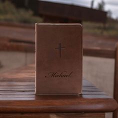 a brown book with a cross on it sitting on top of a wooden bench outside