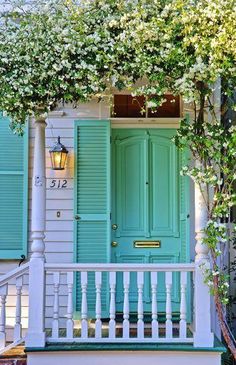 a green door on a white house with vines growing over the front and side porch