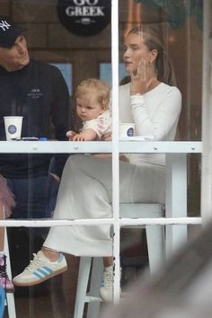 a man and woman sitting at a table with a baby in their lap looking out the window