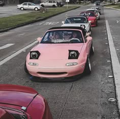 pink sports cars lined up on the side of the road with people in their seats