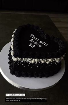 a heart shaped cake with pearls on the edges and black frosting, sitting on a white plate