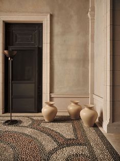 three vases sitting on the floor in front of a doorway with a black door