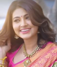 a woman in a pink sari smiling and holding her hand up to her ear