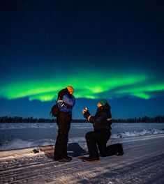 two people sitting in the snow looking at an aurora bore