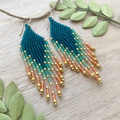 two pairs of beaded earrings on top of a wooden table next to green leaves