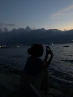 a person sitting on the beach taking a photo with their cell phone at night time