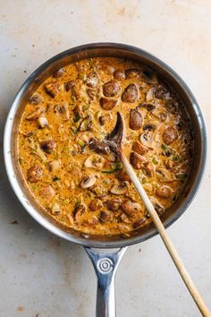 a skillet filled with food on top of a white counter next to a wooden spoon