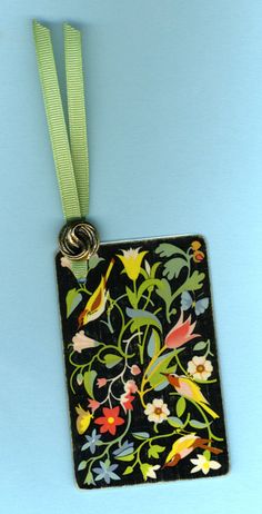 a black square shaped ornament with colorful flowers and leaves on a green ribbon