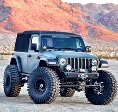 a green jeep parked in the desert with mountains in the backgrounds