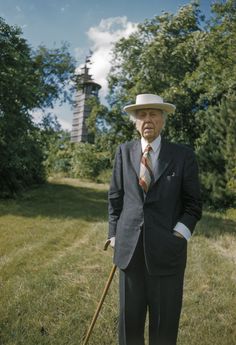 an old man in a suit and tie holding a cane while standing on the grass