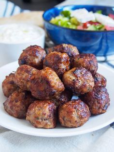 some meatballs on a white plate next to a bowl of salad