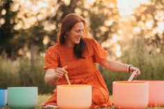 a woman in an orange dress is sitting on the grass and playing with colorful bowls