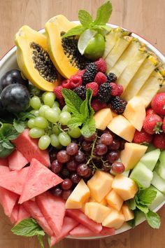 a bowl filled with different types of fruit on top of a wooden table next to watermelon, grapes, kiwi and pears