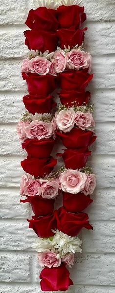 red and pink flowers are arranged on a white brick wall in the shape of a letter