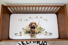 a brown dog sitting in a wooden crib with ducks and watercolors on it