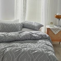 a bed with grey and white comforter in a bedroom next to a window covered by sheer curtains