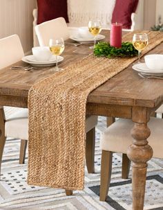 a wooden table topped with white plates and glasses filled with wine sitting on top of a rug