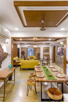 an open concept living room and dining area with wood accents on the ceiling, yellow couches, green table runner, and wooden chairs