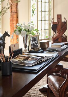 a wooden table topped with lots of books and vases filled with flowers next to a horse figurine