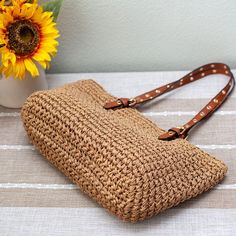 a straw purse sitting on top of a table next to a sunflower