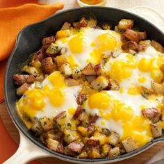 a skillet filled with eggs and potatoes on top of a wooden table next to an orange napkin