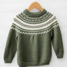 a green and white sweater hanging on a wooden hanger next to a white wall