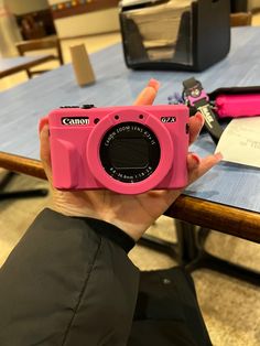 a person holding up a pink camera in front of a table