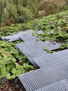 several metal grates are laying on the ground in front of green plants and trees