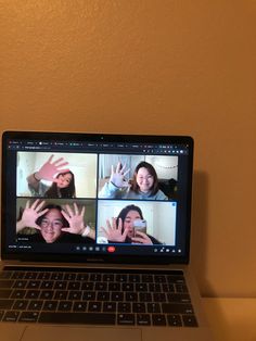 a laptop computer with four people on the screen and one is holding their hands up