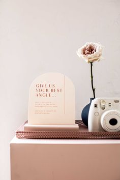 a white flower sitting on top of a table next to a camera and a plaque