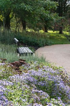 a park bench sitting in the middle of a flower filled area next to a path