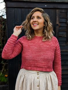 a woman wearing a pink sweater and beige skirt