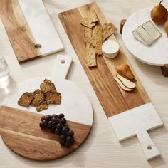 cheese, crackers and grapes sit on cutting boards next to plates with pears