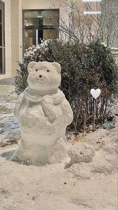 a snowman made to look like a teddy bear in front of a building and shrubbery