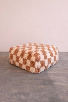 a brown and white checkered dog bed sitting on top of a cement floor next to a wall