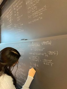 a woman writing on a blackboard in front of a wall with lots of calculations